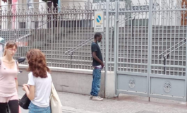 Migrante africano minge in pieno giorno sulla cancellata di una chiesa davanti a donne e bambini